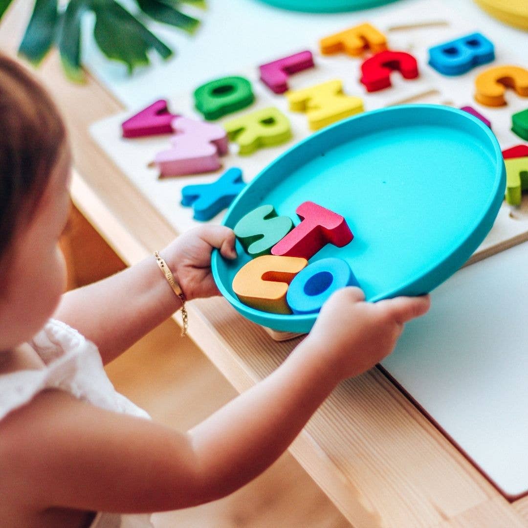 Child playing with colorful alphabet letters on a wooden table and a blue bobo&boo plate