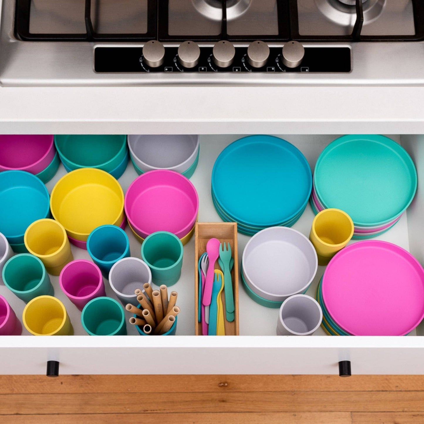 Colorful dishes including plates, cups, and utensils in a kitchen drawer. bobo&boo