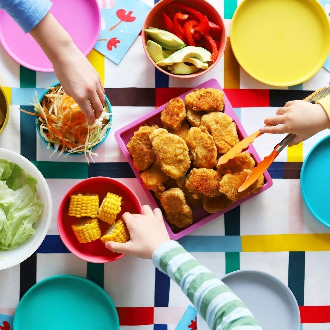 Children's hands reaching for food on a colourful table with various dishes bu bobo&boo