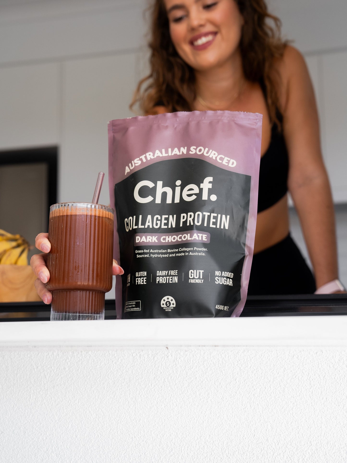 Person holding a glass of dark chocolate protein shake next to a bag of Chief Collagen Protein.