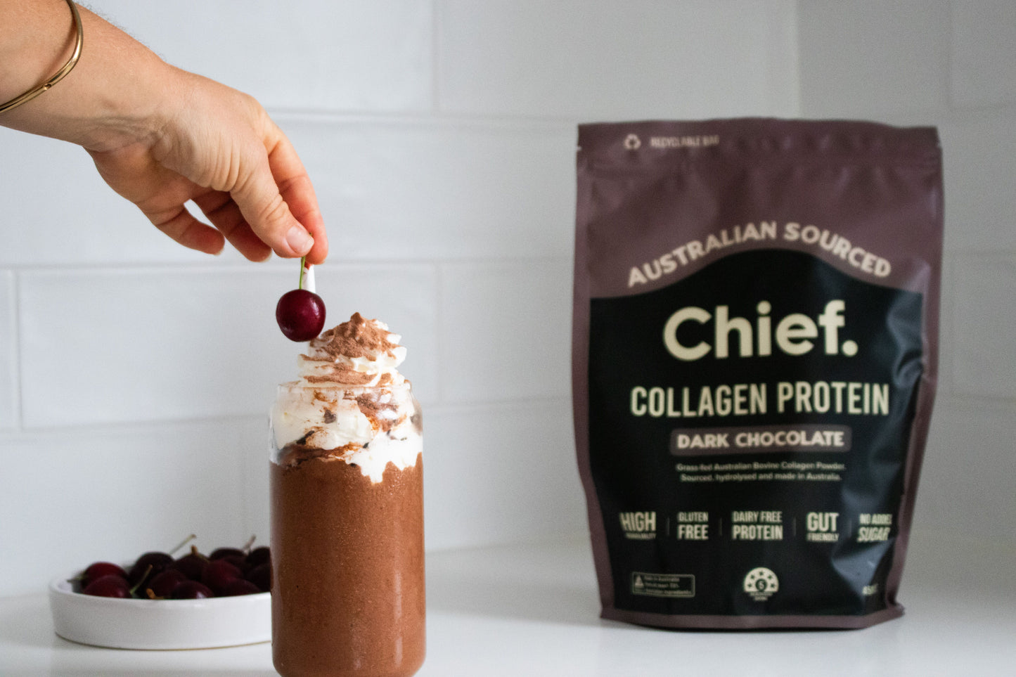 Chocolate protein shake with whipped cream and a cherry, next to a bag of Chief Collagen Protein dark choclate