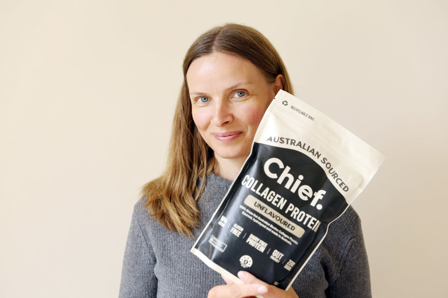 Woman holding a package of Chief unflavoured Collagen Protein against a beige background
