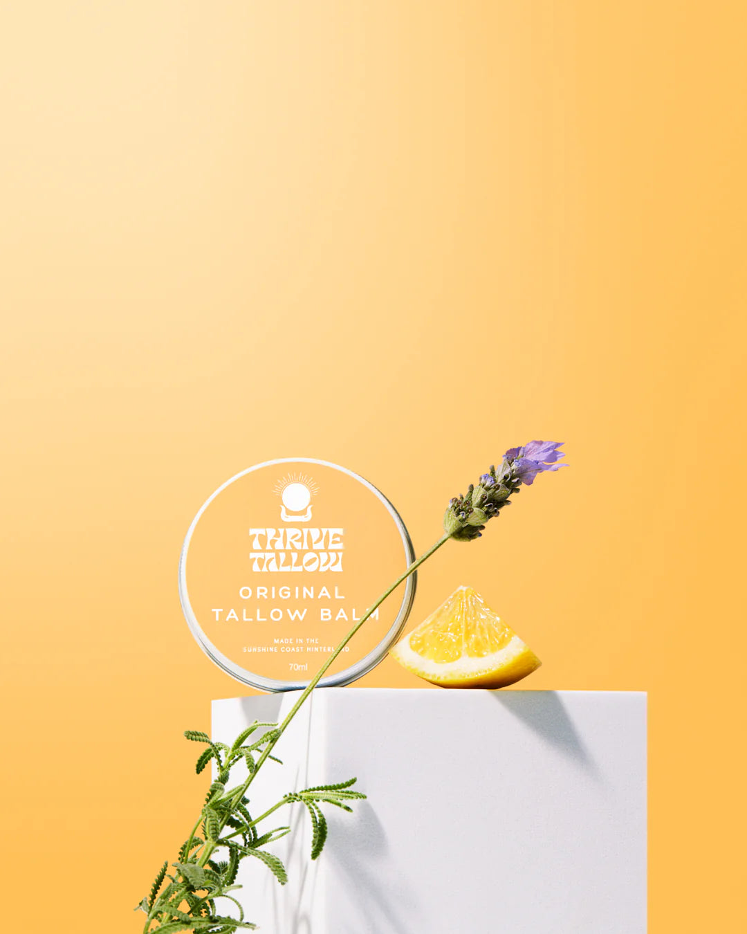 Thrive Tallow balm container with lemon and lavender on a yellow background