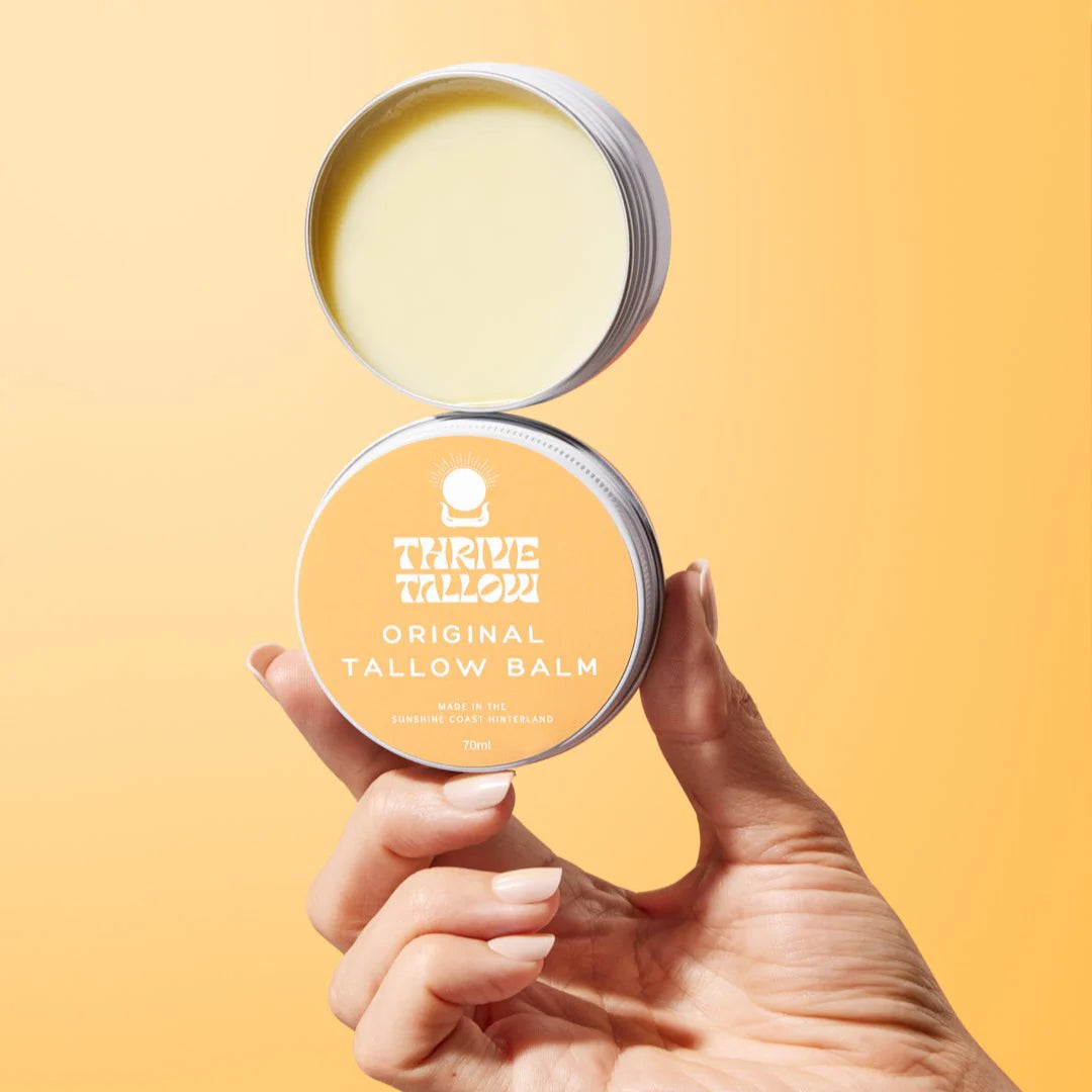 Hand holding an open tin of Thrive Tallow Original Tallow Balm against a yellow background