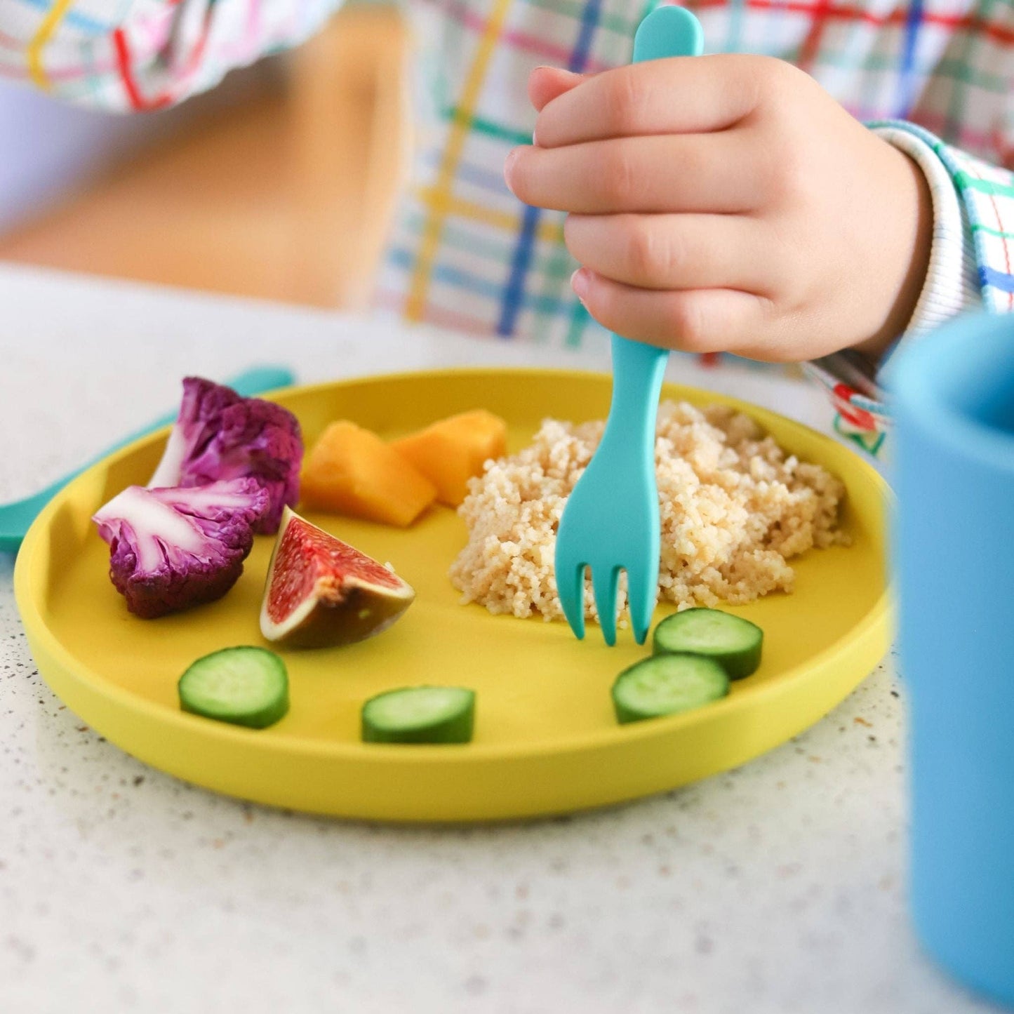 bobo&boo plate. Child's hand holding a blue fork over a plate of food on a yellow plate.