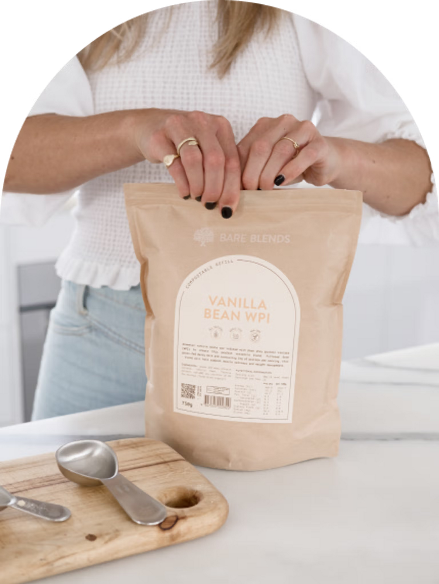 Person holding a bag of vanilla bean WPC by Bare Blends on a white surface with a wooden cutting board.