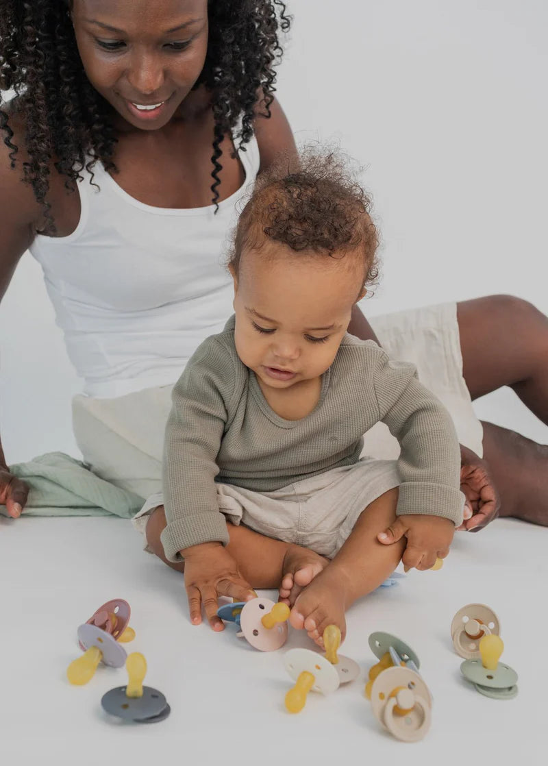 Woman and child playing with BIBS pacifiers on a white surface