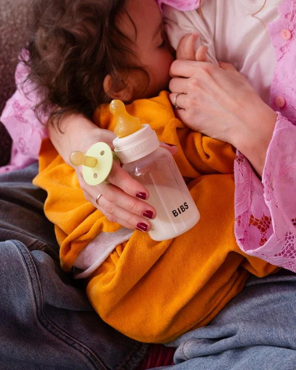 Person holding a BIBS baby bottle and a BIBS pacifier , surrounded by soft lighting.