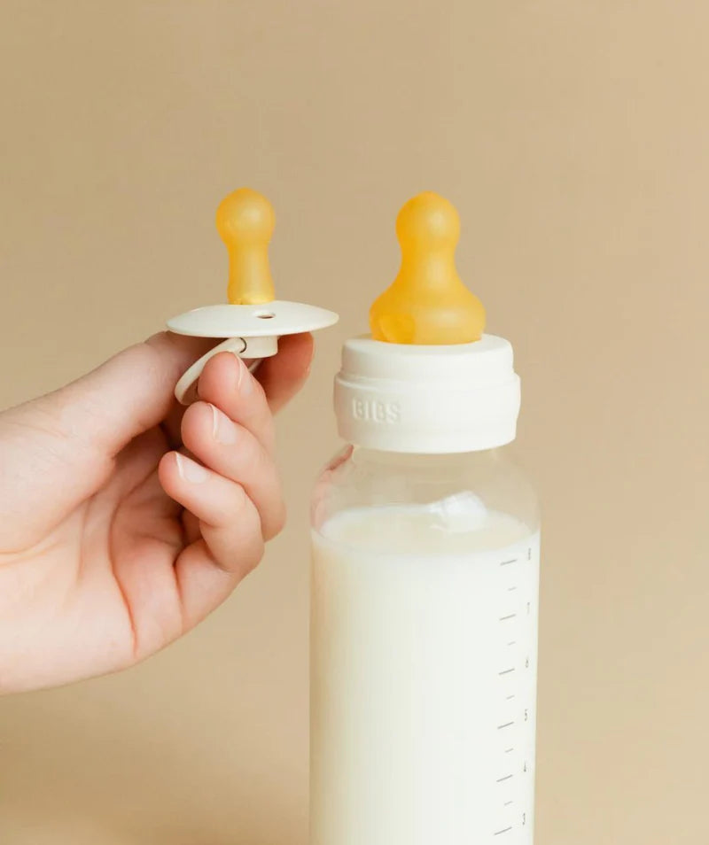 BIBS glass bottle and dummy held on beige backround