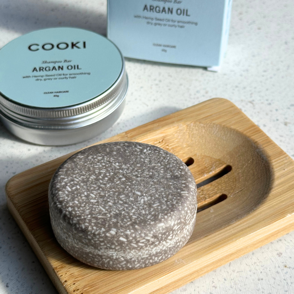 Cooki Argan Oil shampoo bar on a wooden soap dish with packaging in the background.