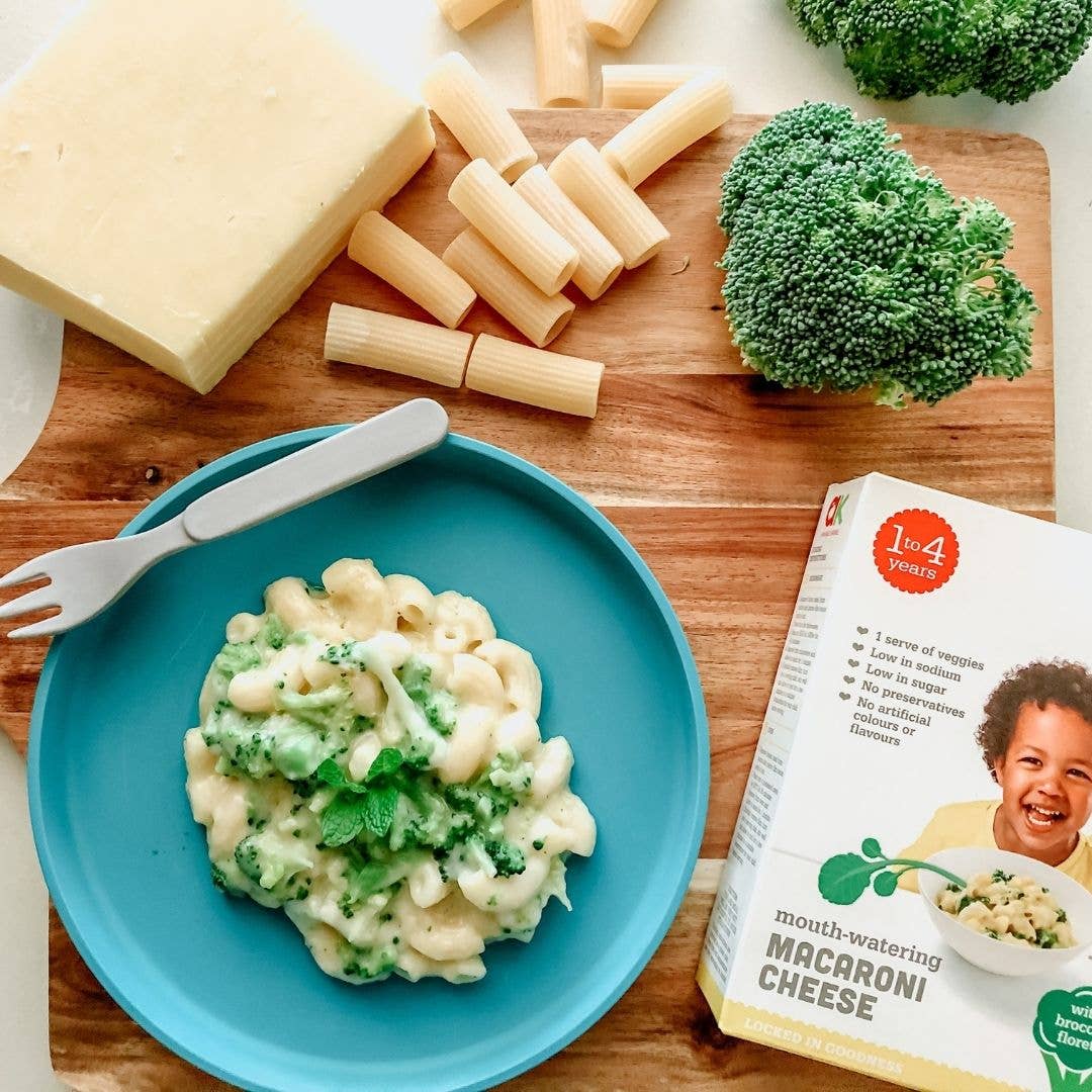 Macaroni and cheese with broccoli on a blue plate, surrounded by ingredients and a box of macaroni and cheese. bob&boo