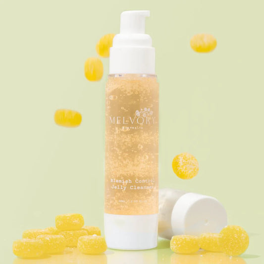 Melvory skincare Blemish Control Jelly Cleanser in a clear pump bottle with a white cap, surrounded by scattered yellow gummy candies on a light green background.
