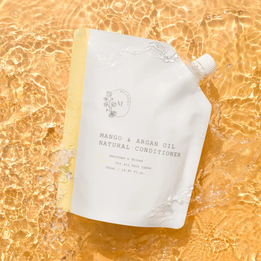 A white stand-up pouch of Melvory Natural Conditioner in Mango & Argan Oil, styled on a golden, water-textured background.