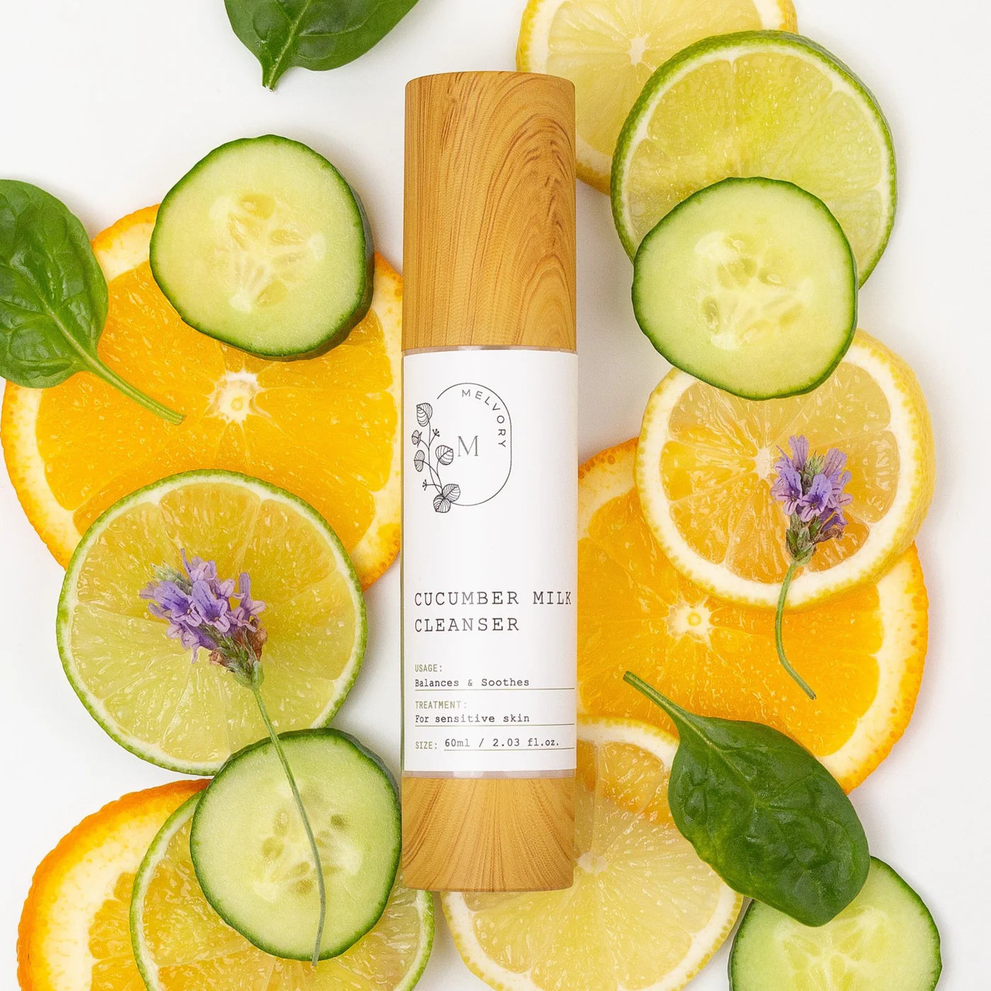 Melvory Cucumber milk cleanser bottle surrounded by sliced cucumbers, oranges, and limes on a white background.
