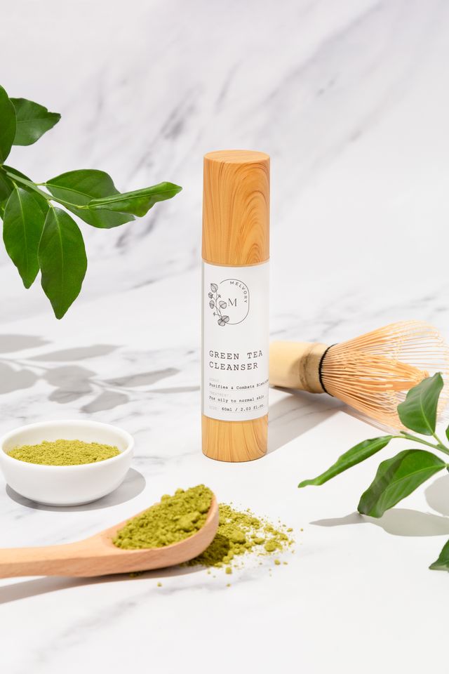 melvory Green tea cleanser with wooden scoop and leaves on a marble background