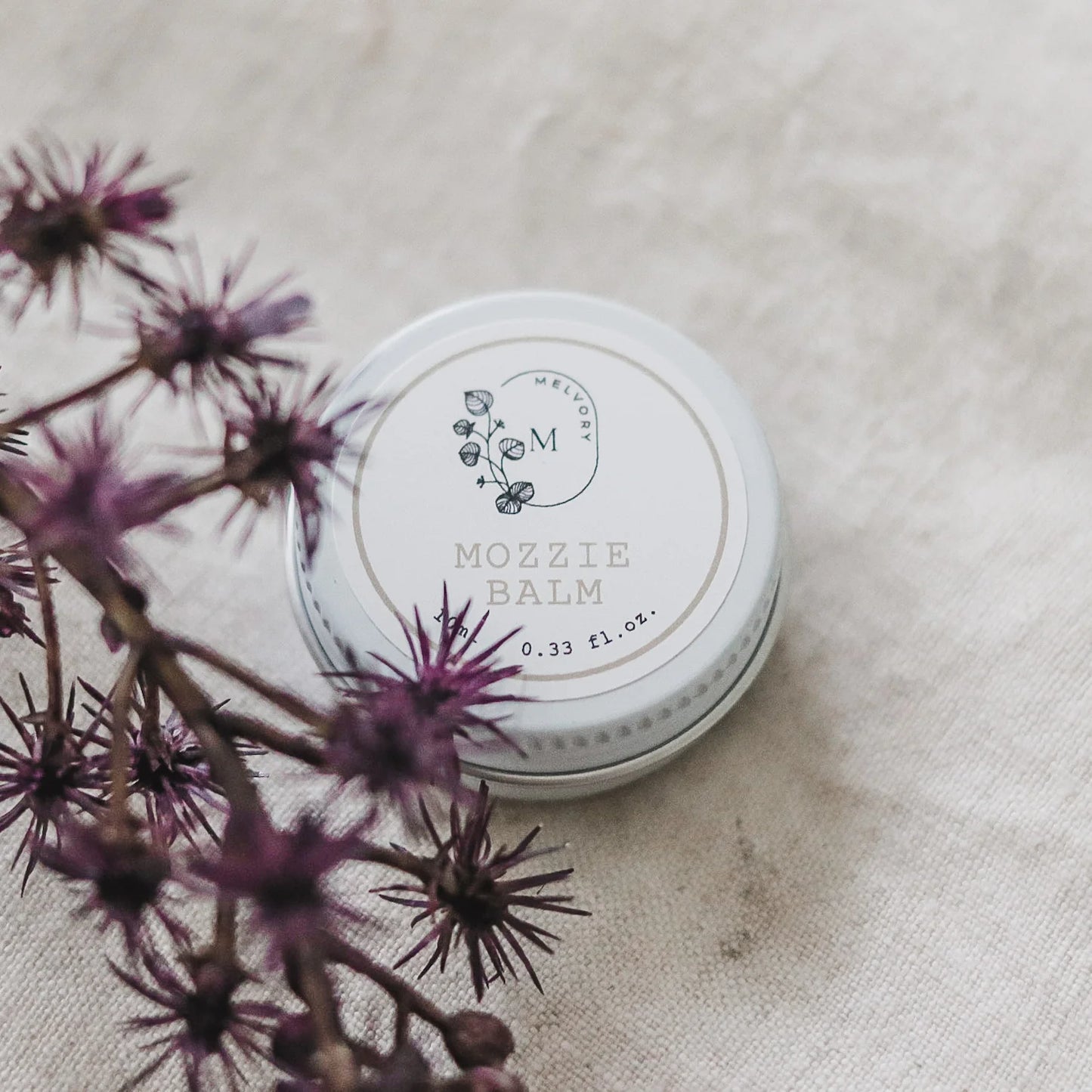 melvory skincare Mozzie Balm container on a textured surface with purple flowers
