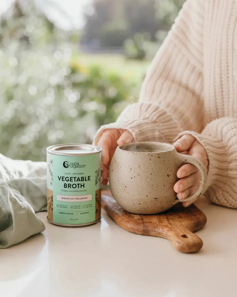 nutra organics vegetable broth canister with a lady holding a mug of hot broth