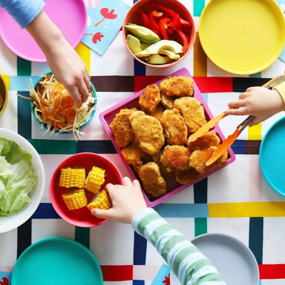 Children's hands reaching for food on a colourful table with various dishes bu bobo&boo