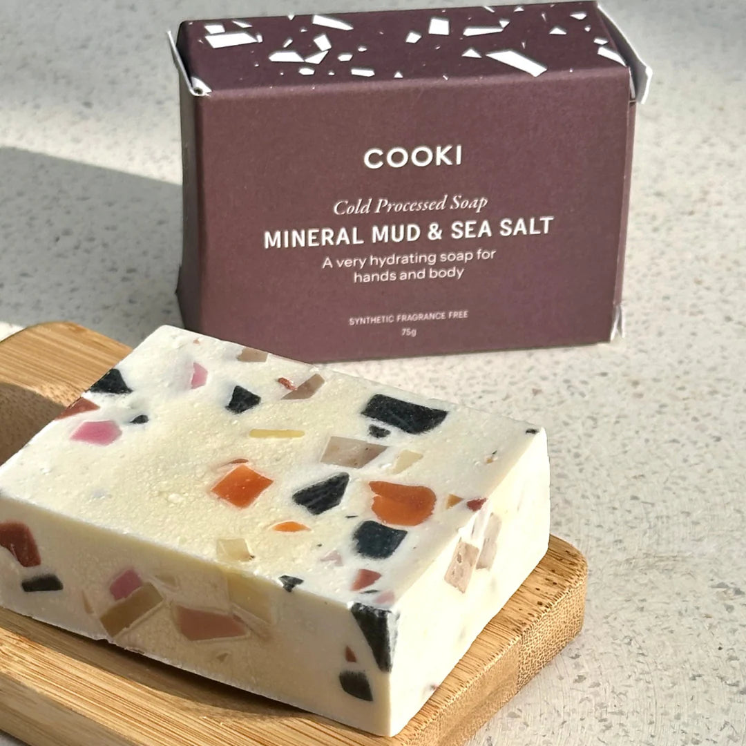 Cooki mineral mud & sea salt soap on a wooden board with packaging in the background.