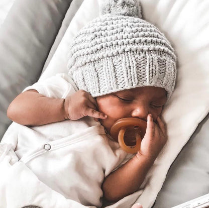 Baby sleeping with a natural rubber soother and wearing a knitted hat