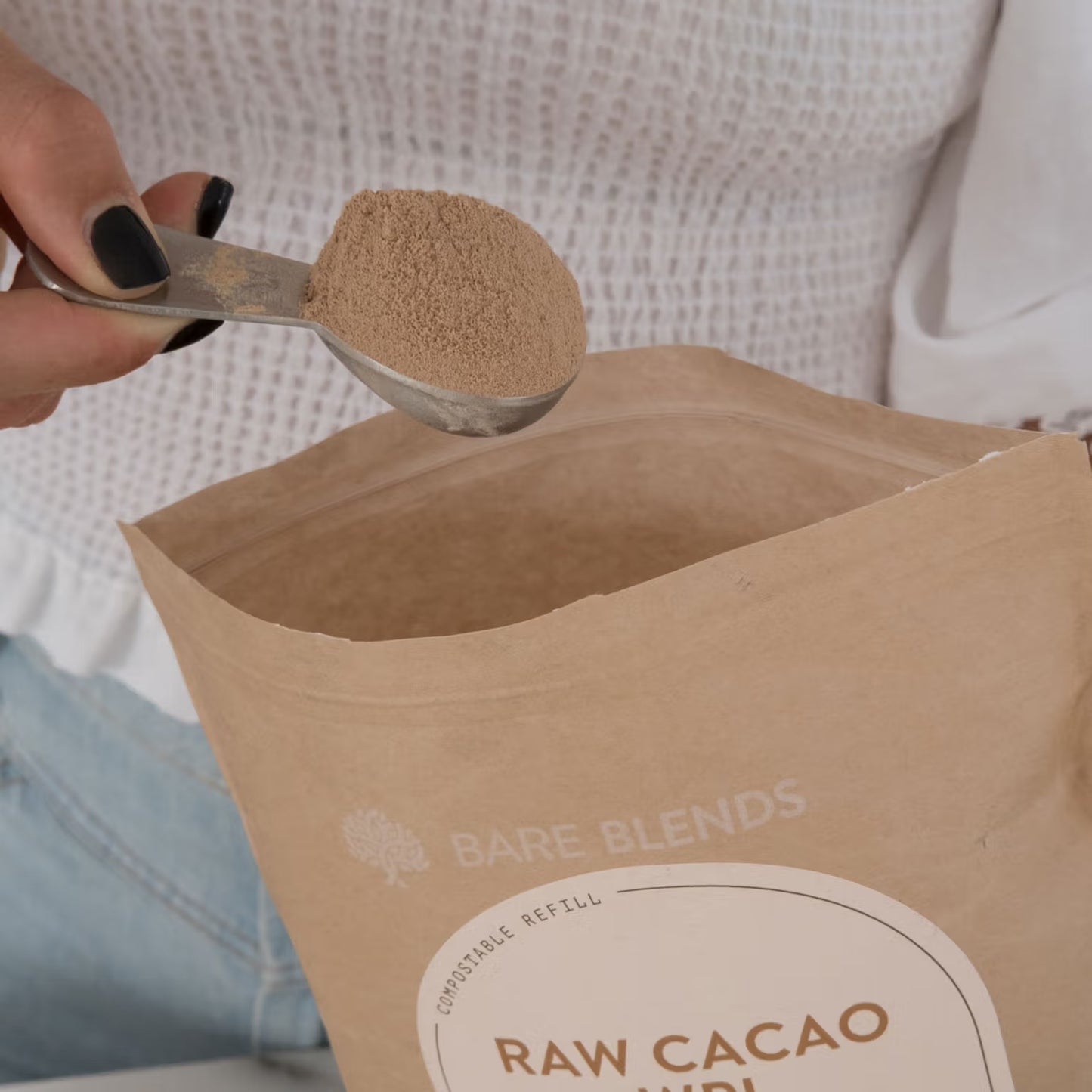 Raw cacao powder being measured with a scoop from a Bare Blends raw cacao powder bag.
