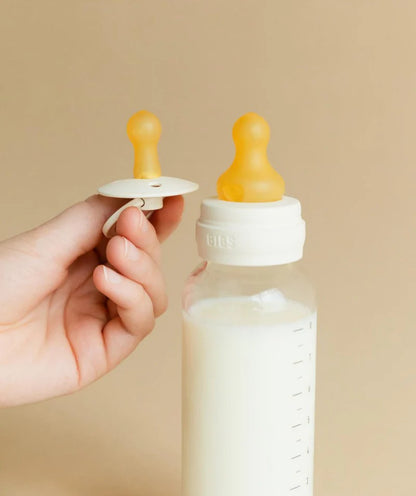 BIBS Baby bottle with natural rubber teat and a bibs pacifier held by a hand against a beige background