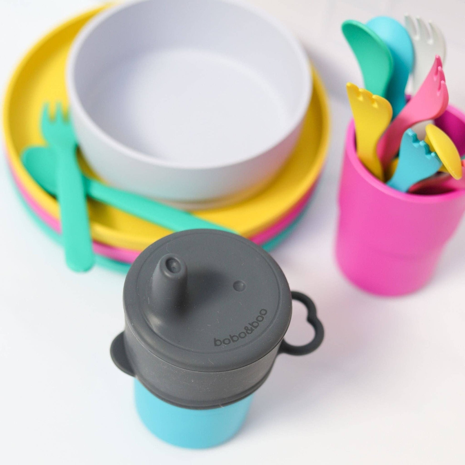 Colorful children's tableware by bobo&boo  including bowls, plates, cups, and utensils on a white background.