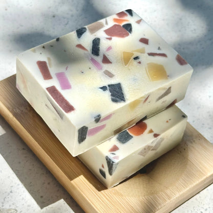 Two terrazzo-patterned cooki haircare soap bars stacked on a wooden board with a marble background.
