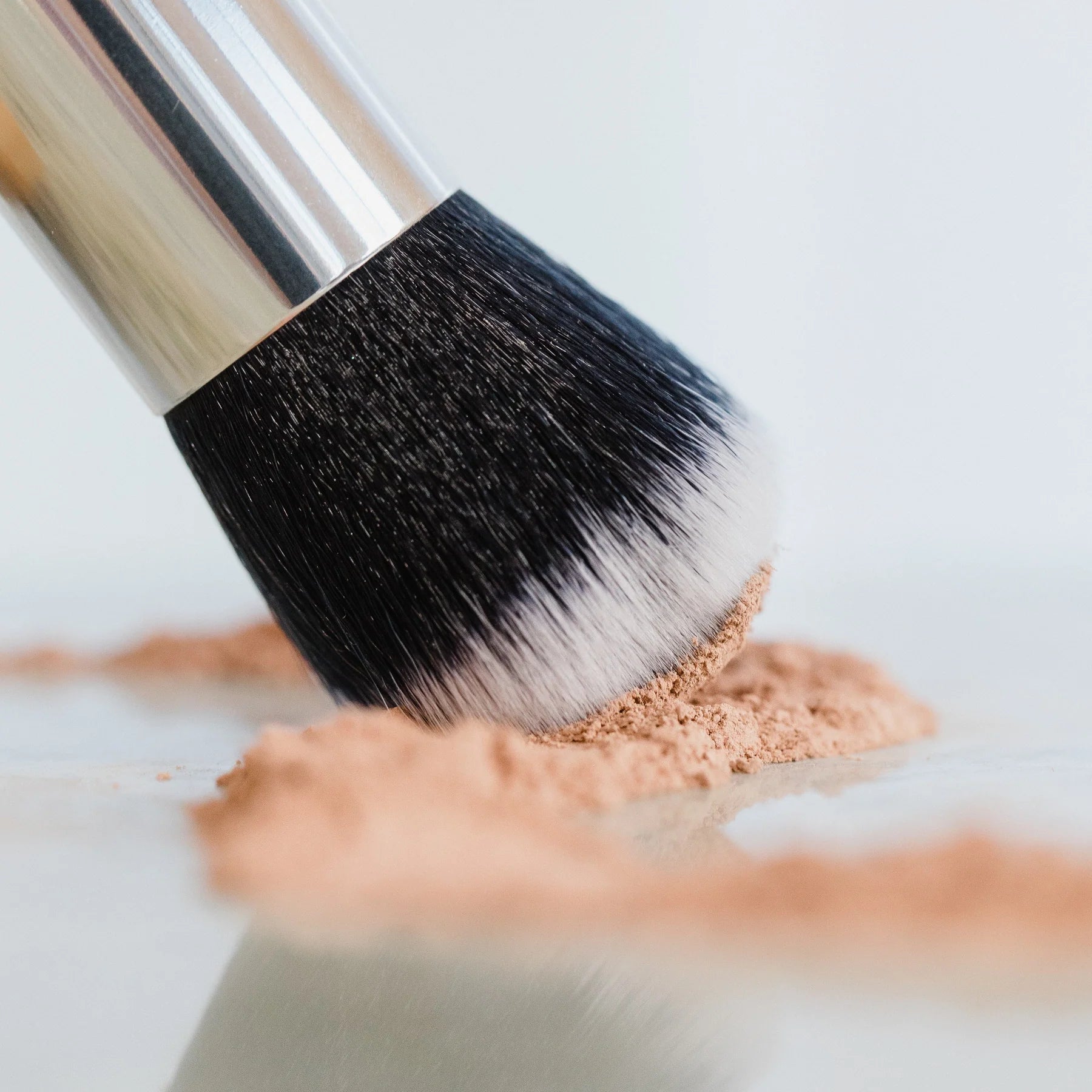 melvory Makeup kabuki brush dipping into mineral powder on a light background