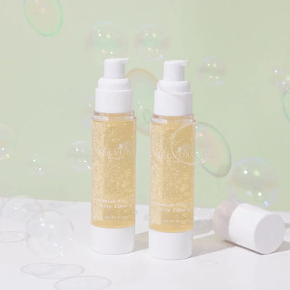 Two bottles of  melvory blemish control Cleanser with a white cap, filled with a sparkling pale yellow liquid, standing on a white surface with a light green background and floating bubbles.