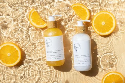Two bottles of Melvory shampoo and conditioner with orange slices on a water surface